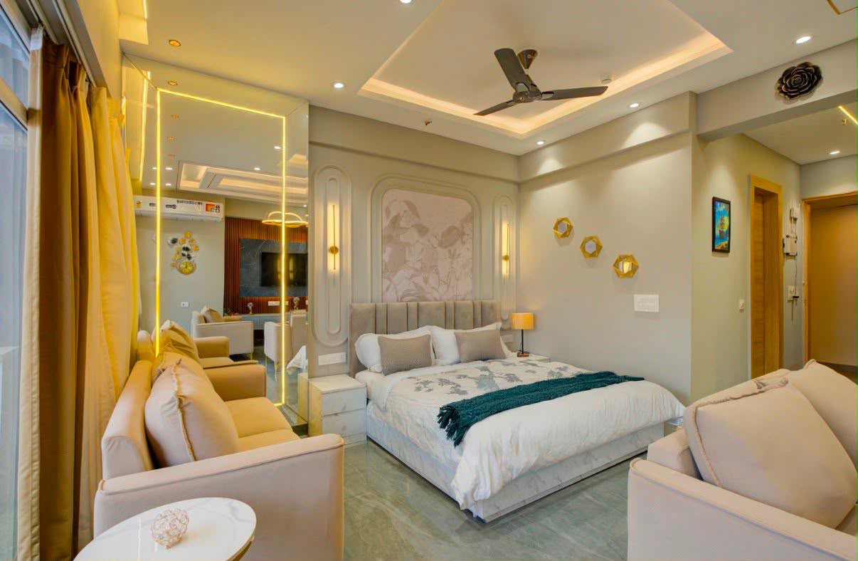 Furnished studio with a bed, velvet headboard, wall lights and a two-seater sofa beside a mirrored panel